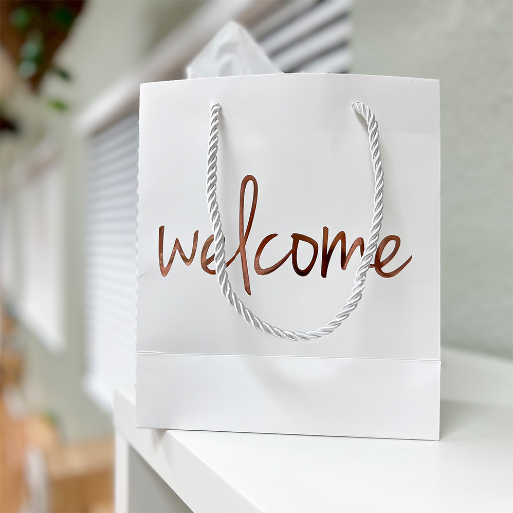 White, welcome back with welcome written in cursive in gold sitting on a shelf